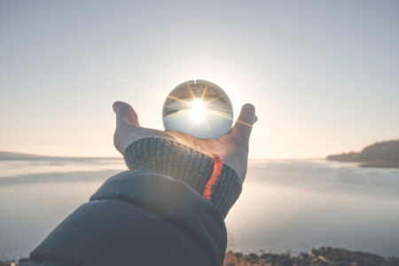 Hand holding a crystal ball in the winter sunrise by a lake in the morning